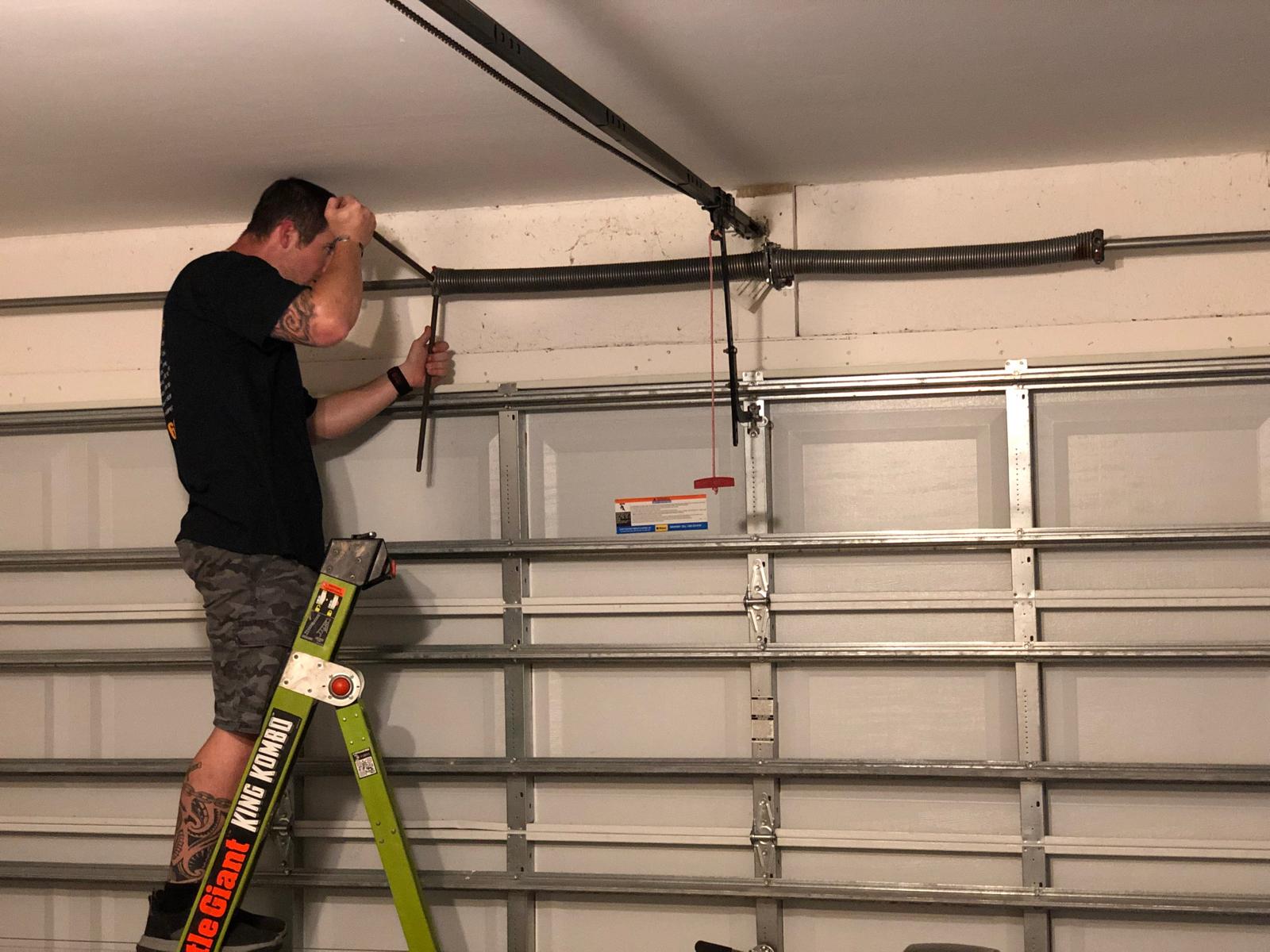 A licensed technician using winding bars on a loaded torsion spring